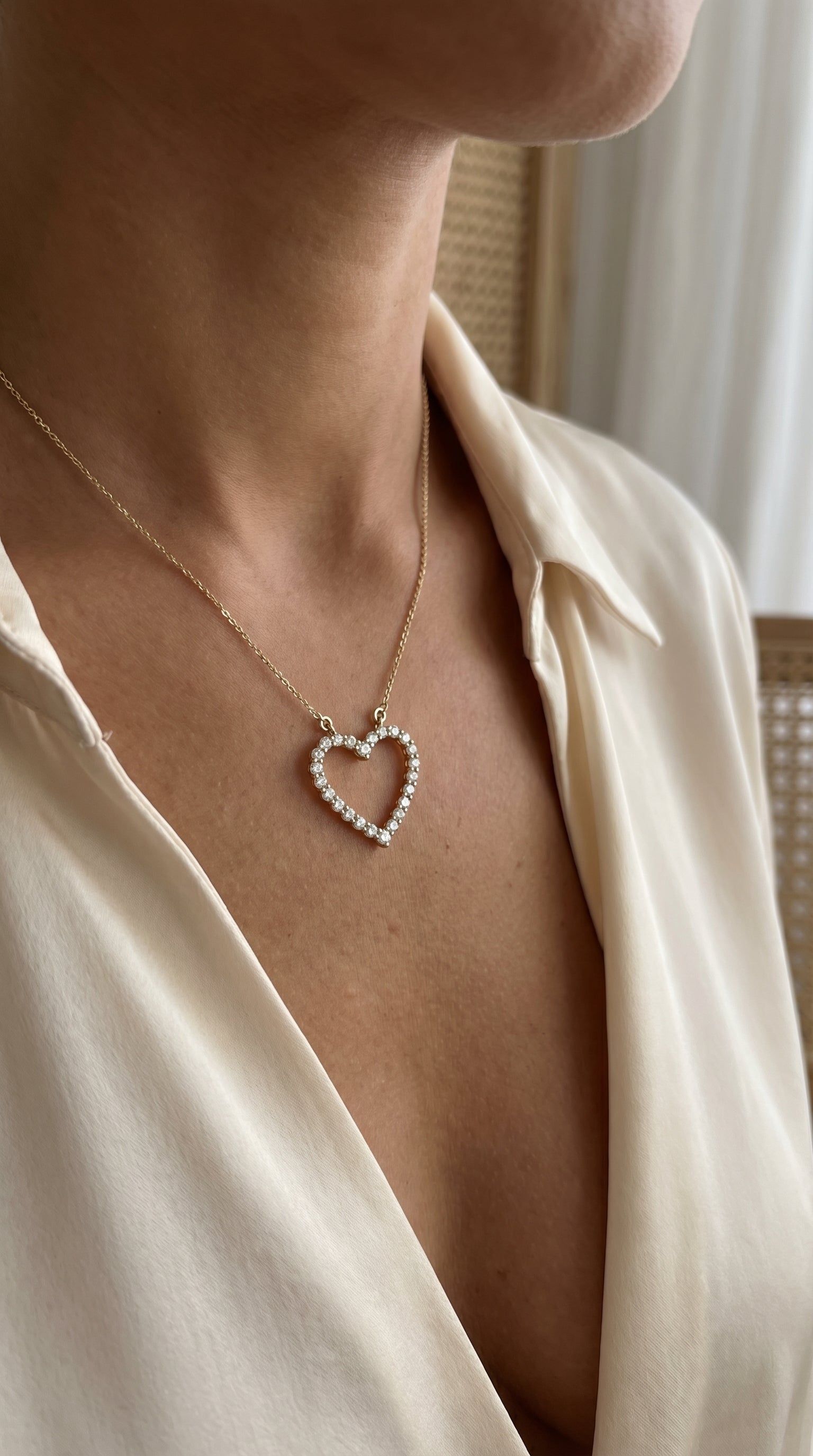 Necklace with a heart-shaped pendant worn by a person in a beige shirt.