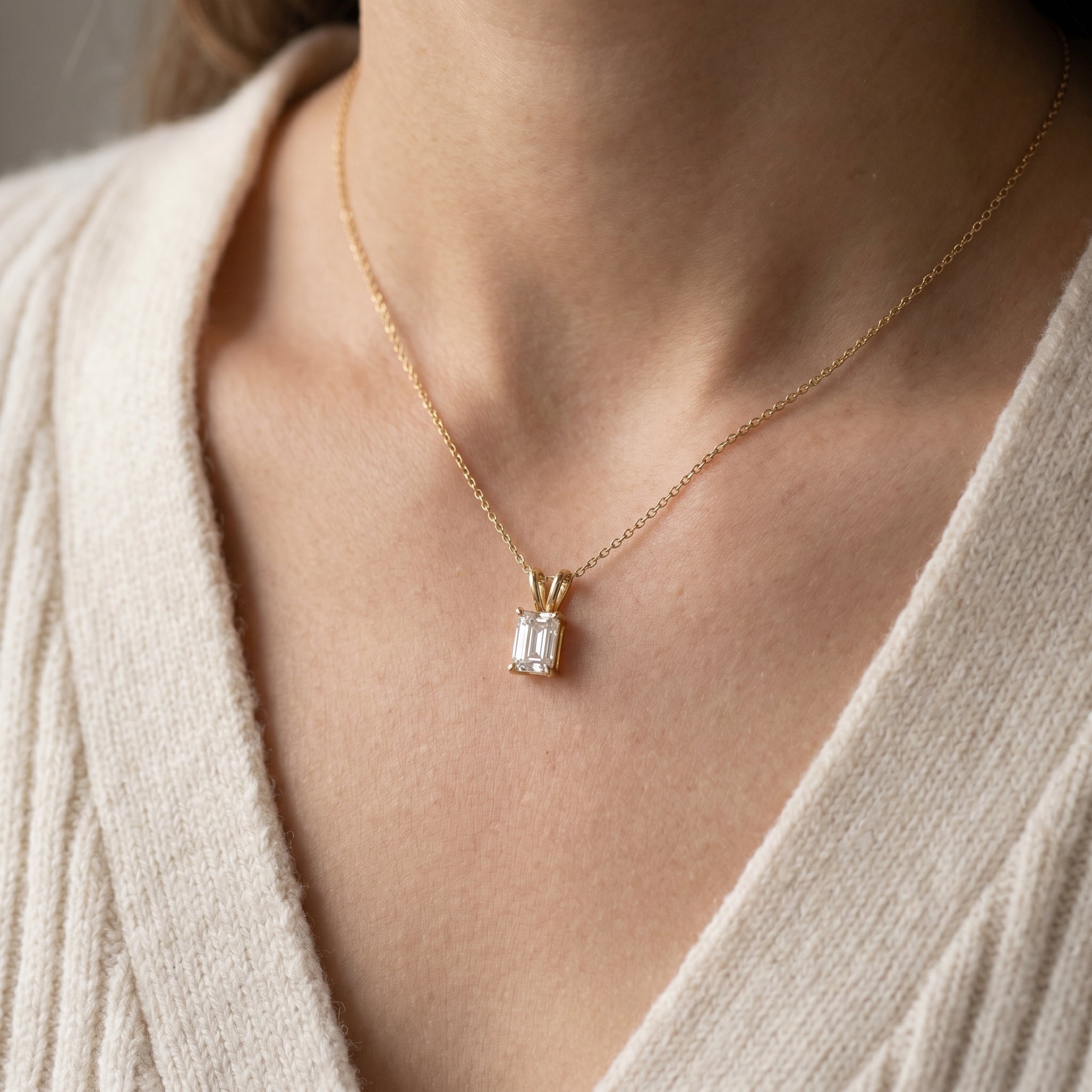 Gold necklace with a diamond pendant worn by a person in a beige sweater.