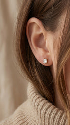 Close-up of an ear wearing a diamond earring with a neutral background