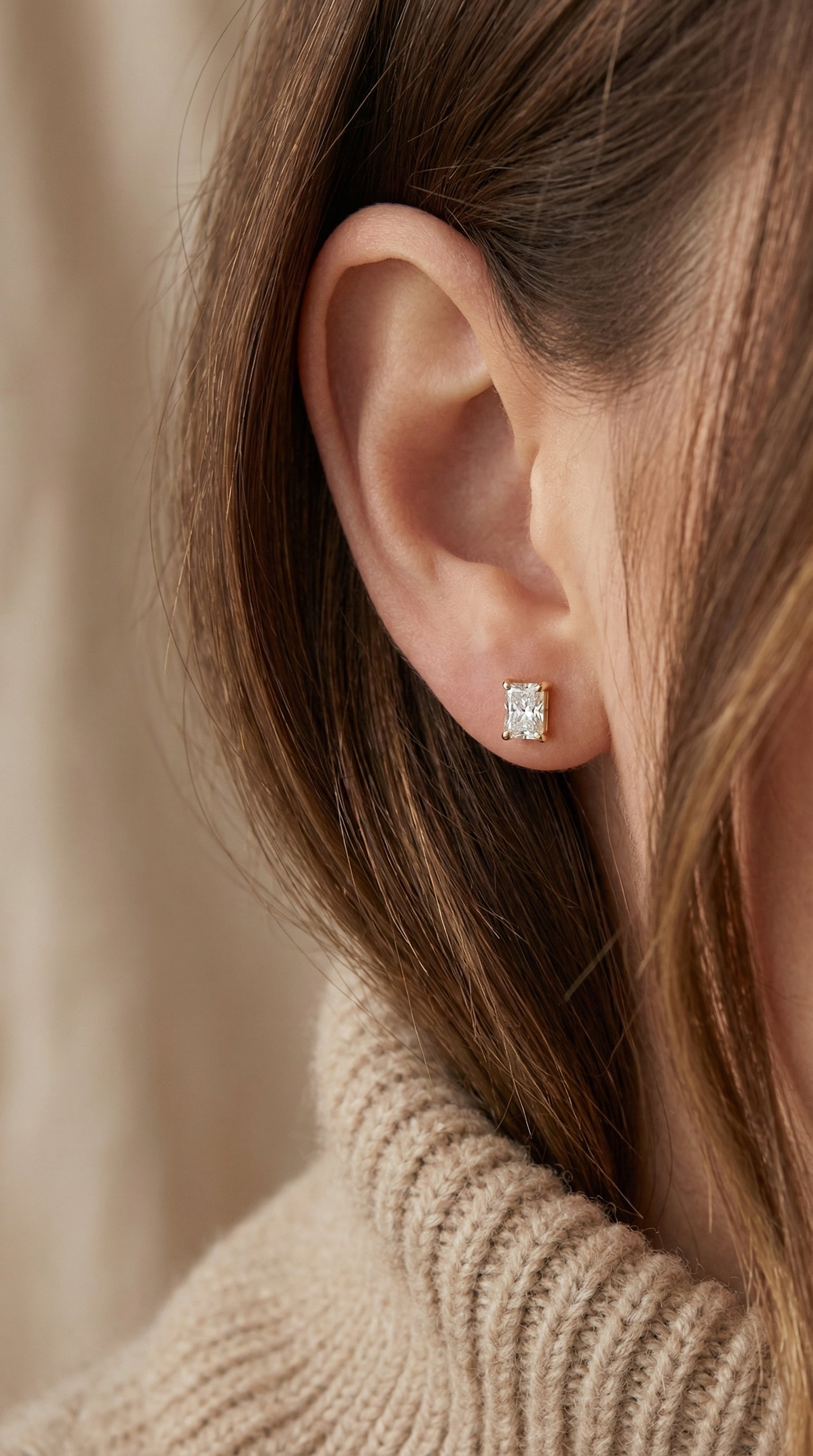 Close-up of an ear wearing a diamond earring with a neutral background