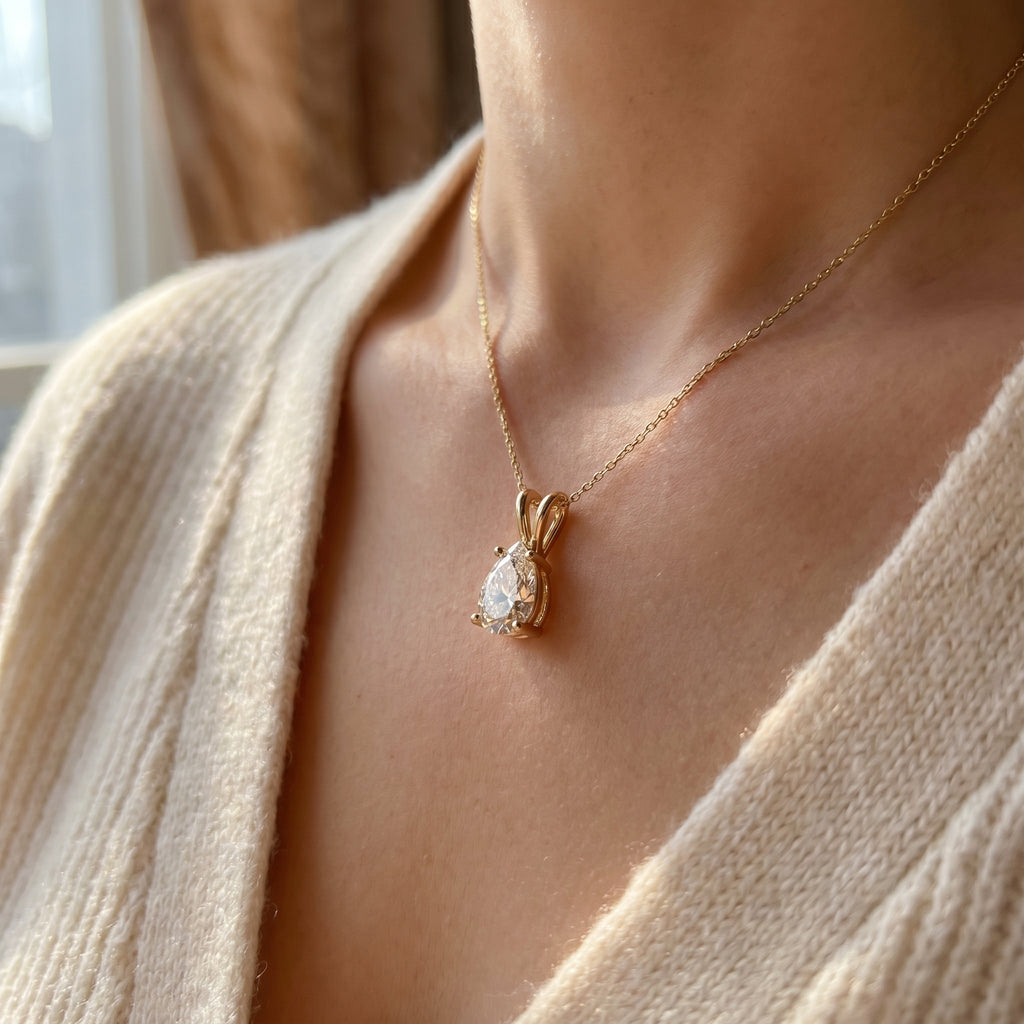 Necklace with a teardrop-shaped pendant worn by a person in a beige sweater.