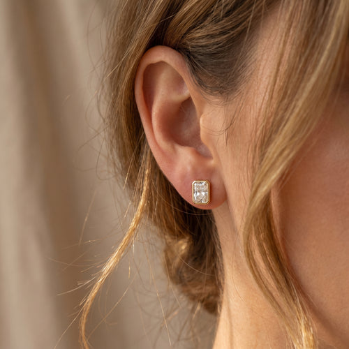 Close-up of an ear wearing a diamond earring with a neutral background