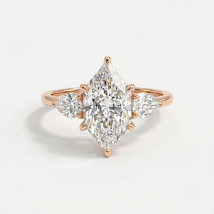 Marquise cut three stone diamond engagement ring with pear side diamonds in polished gold setting on white background
