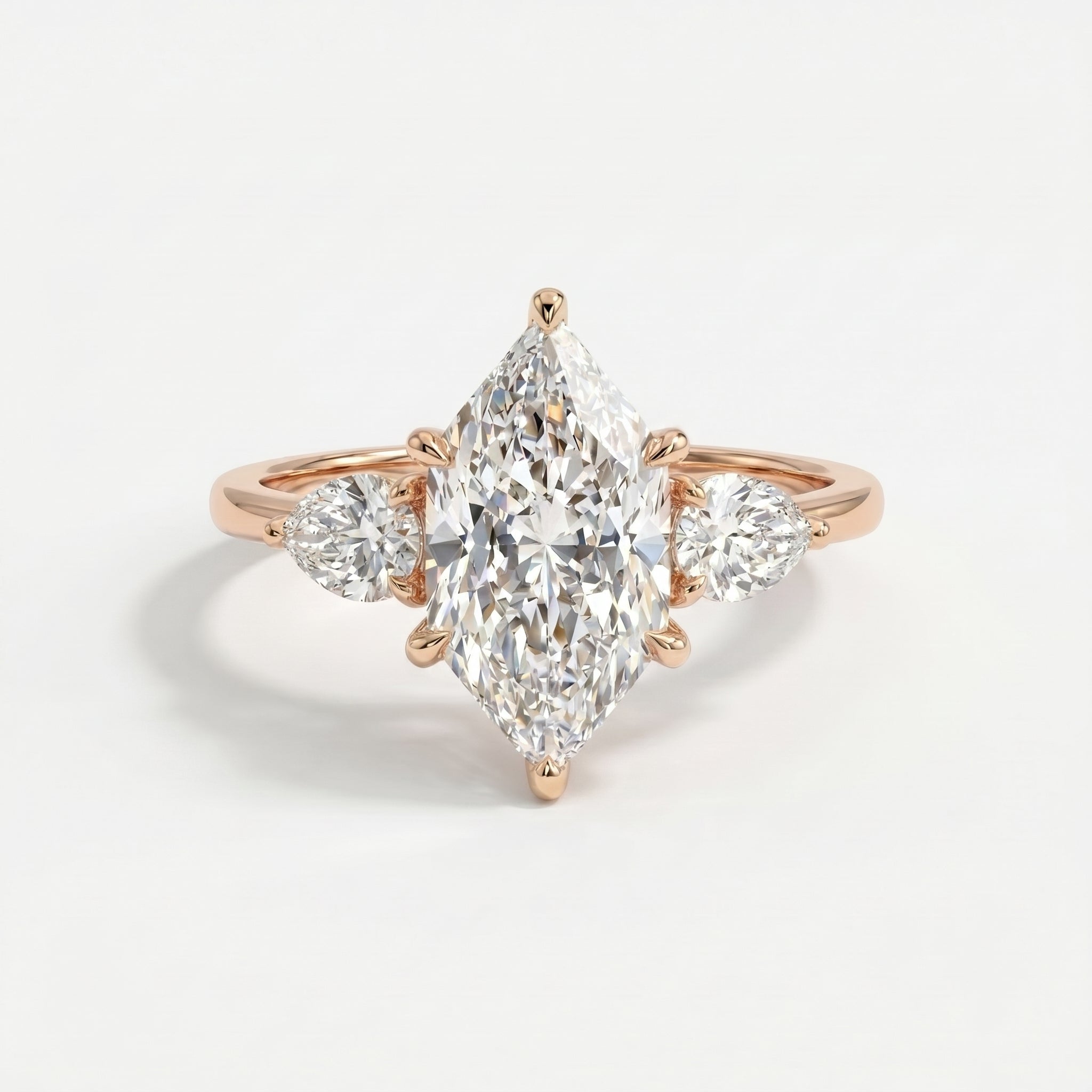 Marquise cut three stone diamond engagement ring with pear side diamonds in polished gold setting on white background