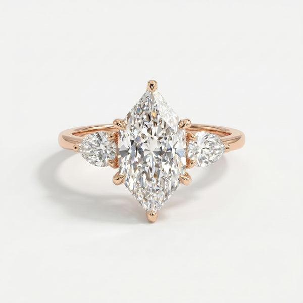 Marquise cut three stone diamond engagement ring with pear side diamonds in polished gold setting on white background