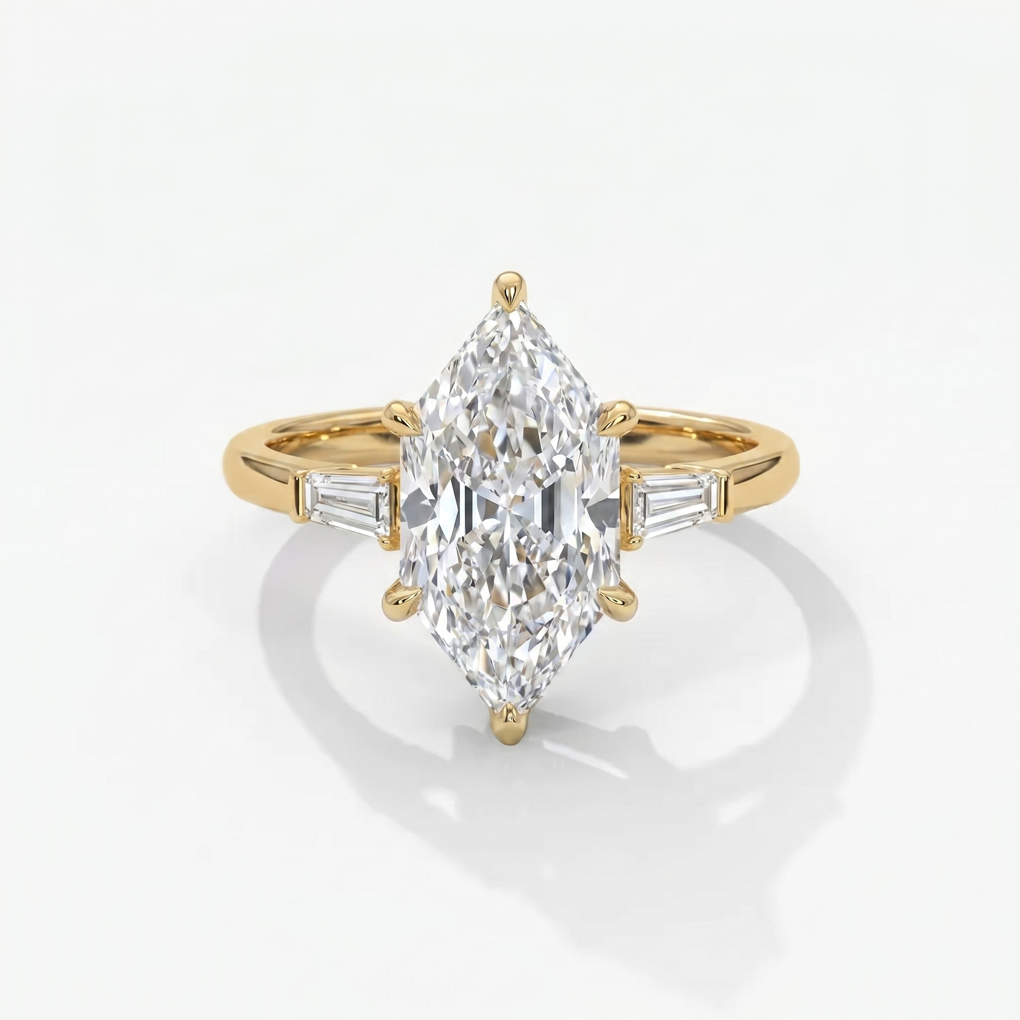 Marquise diamond engagement ring with tapered baguette side stones in polished yellow gold on white background