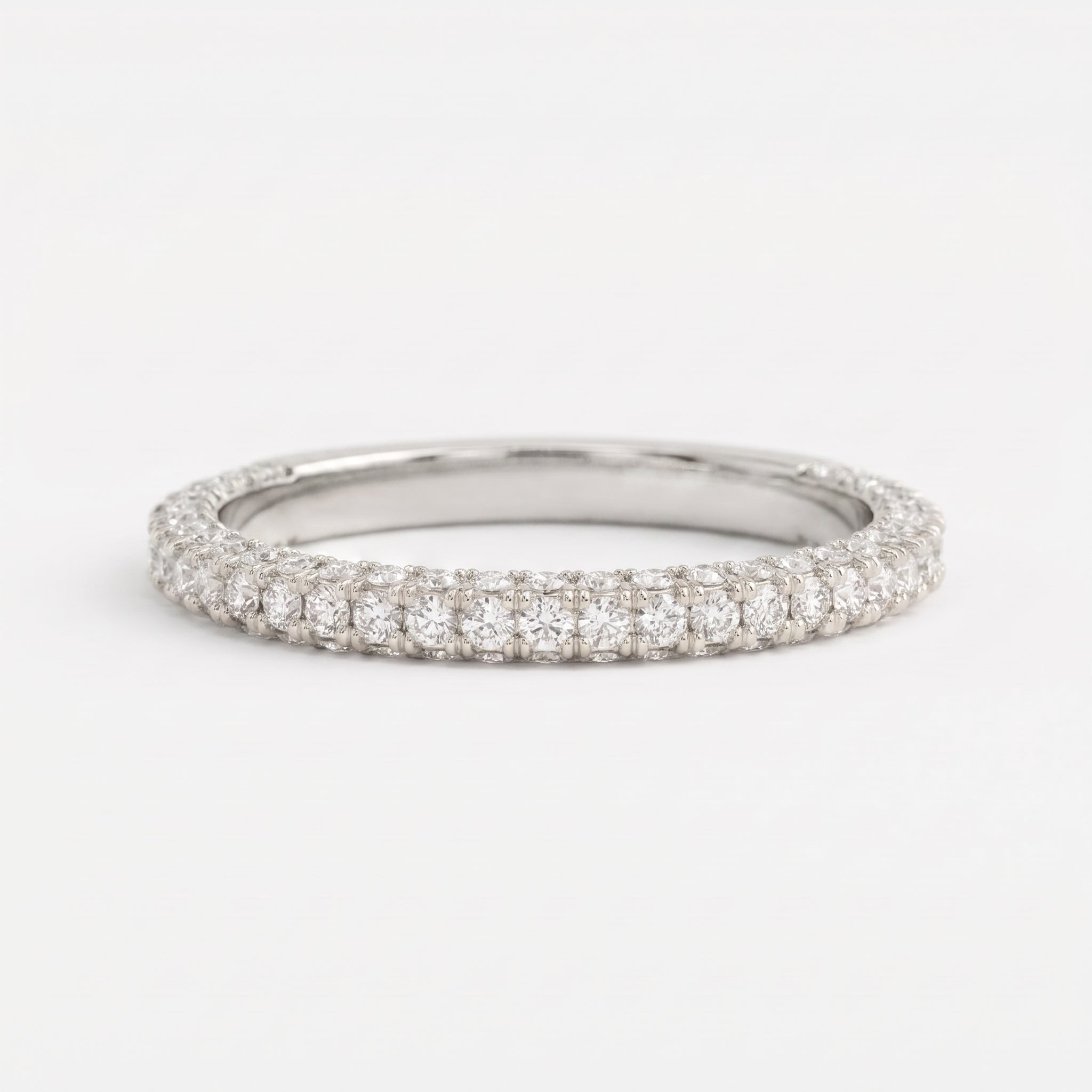 Round brilliant diamond eternity wedding band in polished white gold with shared prong setting on a clean white background.